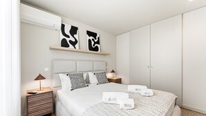 Ein modernes Hotelzimmer mit Bett, Nachttischen, einem Kleiderschrank und abstrakter Wandkunst.