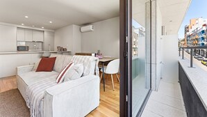Eine moderne Wohnung mit Wohnbereich, einer Küchenzeile und einem Balkon mit Blick auf die Stadt.