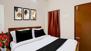 A hotel room with a bed, a nightstand, a potted plant, and three framed artworks on the wall. - Saver Double RKH Inn (Chennai)