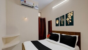 A bedroom with a bed, a wall-mounted air conditioner, a bedside shelf, and three framed leaf artworks. - Saver Double RKH Inn (Chennai)