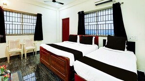 A hotel room with two beds, a desk, chairs, a ceiling fan, and windows with bars. - Super Deluxe Room Ruthran Guest House (Tirukalukundram)
