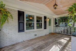 Ein überdachter Balkon mit weißen Backsteinmauern, schwarzen Fensterläden und Holzboden.
