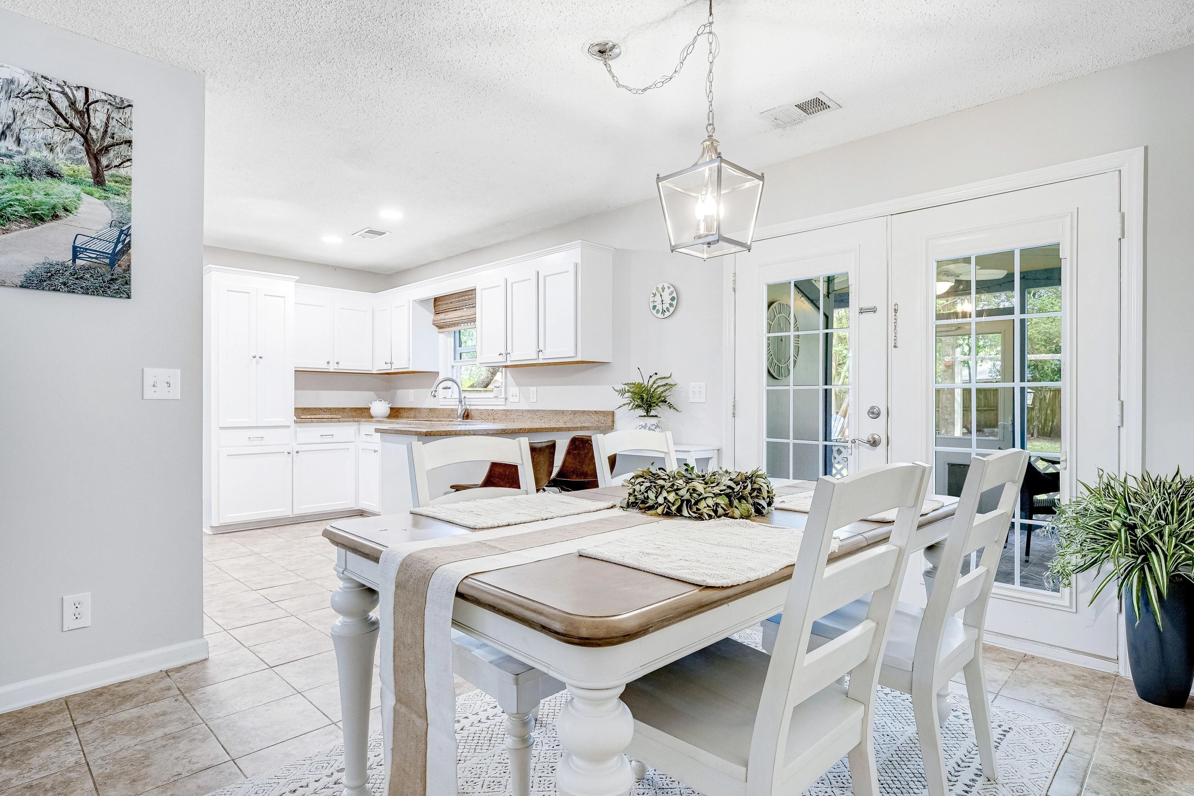 A dining area with a table, chairs, a hanging light fixture, and a view of the kitchen.