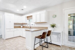 A kitchen with white cabinets, a granite countertop, a sink, and two bar stools. - Coastal Charleston Retreat Near Folly Beach Fun (Charleston)