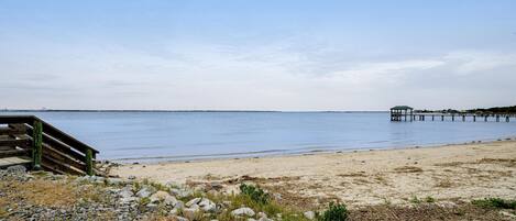 A beach with a wooden walkway leading to a pier.