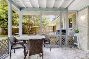 A covered patio with a round table and wicker chairs, a brick wall, and a wooden fence in the background. - Coastal Charleston Retreat Near Folly Beach Fun (Charleston)