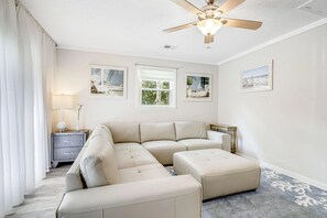 Ein modernes Wohnzimmer mit einem Ecksofa, einem Deckenventilator und gerahmten Kunstwerken an den Wänden.