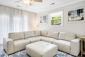 A sectional sofa with a matching ottoman, a ceiling fan, and a window with a view of greenery. - Coastal Charleston Retreat Near Folly Beach Fun (Charleston)