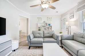 A living room with a grey sofa, a white coffee table, a ceiling fan, and a TV mounted on the wall. - Coastal Charleston Retreat Near Folly Beach Fun (Charleston)