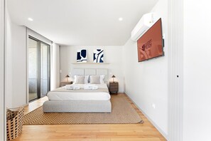 Ein modernes Hotelzimmer mit einem großen Bett, einem Flachbildfernseher und einer Schiebeglastür nach draußen.