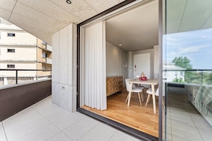 Eine moderne Wohnung mit einer Schiebetür zum Balkon, einem Essbereich mit Tisch und Stühlen sowie Blick auf benachbarte Gebäude.