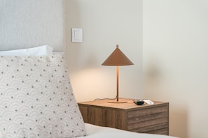 A neatly made bed with a patterned pillow, a bedside lamp, a remote control, and a wall socket. - GuestReady - Aires Prime - G (Porto)