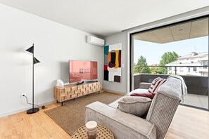 A modern living room with a flat-screen TV, a wooden console, a sofa, a floor lamp, and a large window with a view of buildings. - GuestReady - Aires Prime - G (Porto)