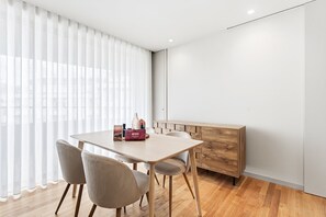 A modern hotel room with a wooden dining table, two chairs, a bench, and a large window with sheer curtains. - GuestReady - Aires Prime - G (Porto)
