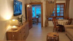Ett vardagsrum med en soffa, ett matbord med stolar, en tv som är monterad på väggen och ett träskåp.