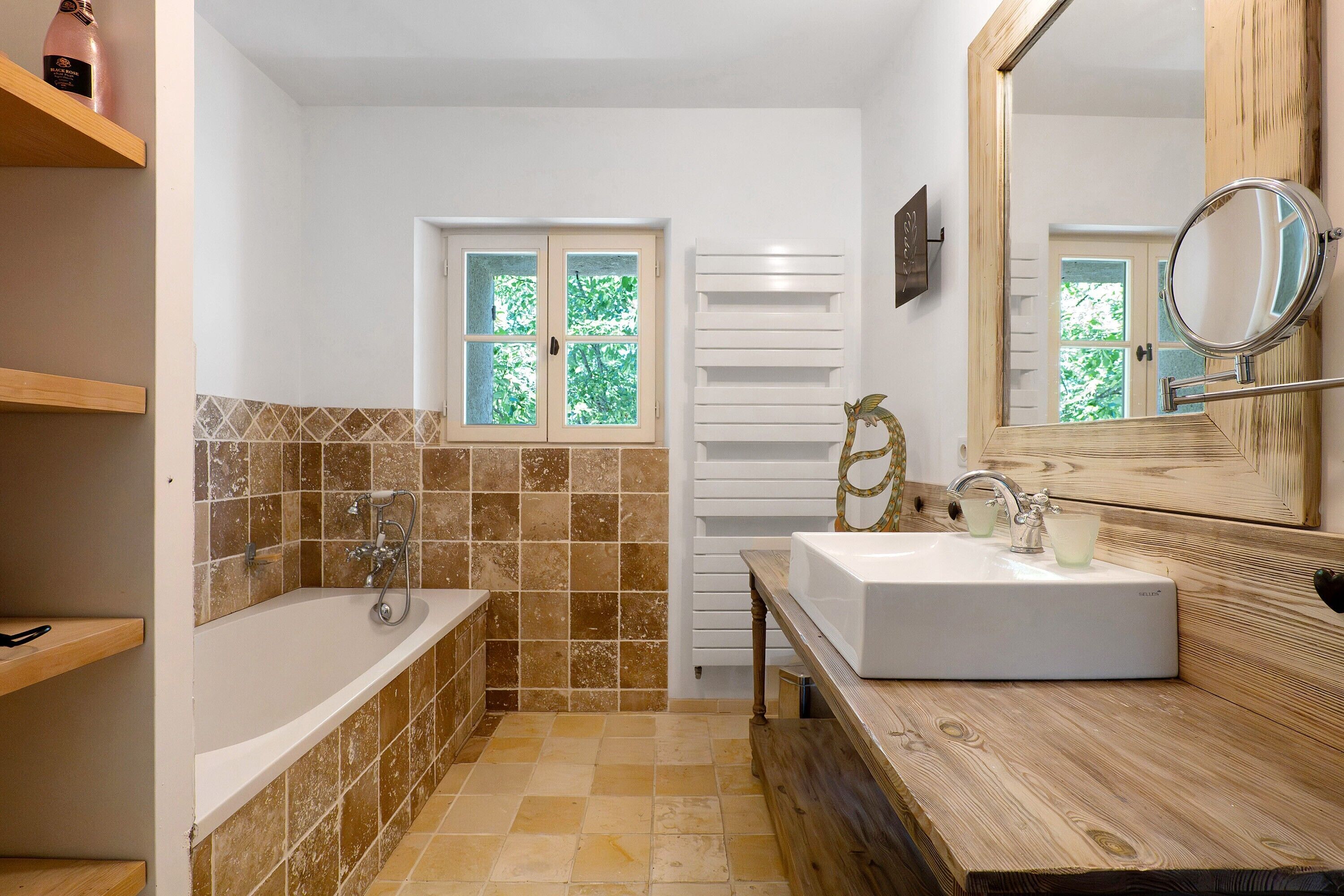 A bathroom with a bathtub, a sink, and a mirror. There is a window with a view of trees.