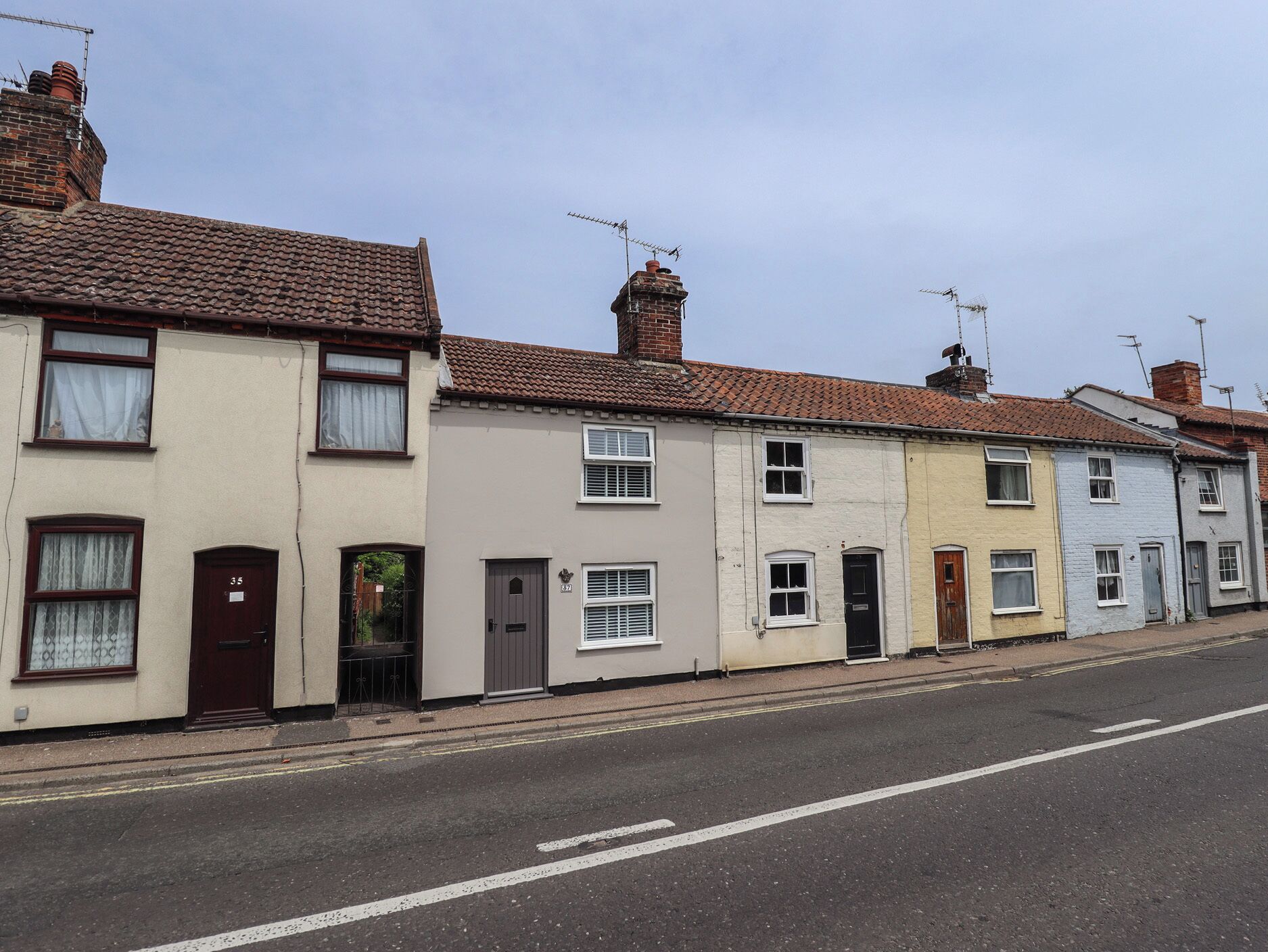 A row of terraced houses with distinct front doors and windows, a clear road in front, and no visible amenities or features.