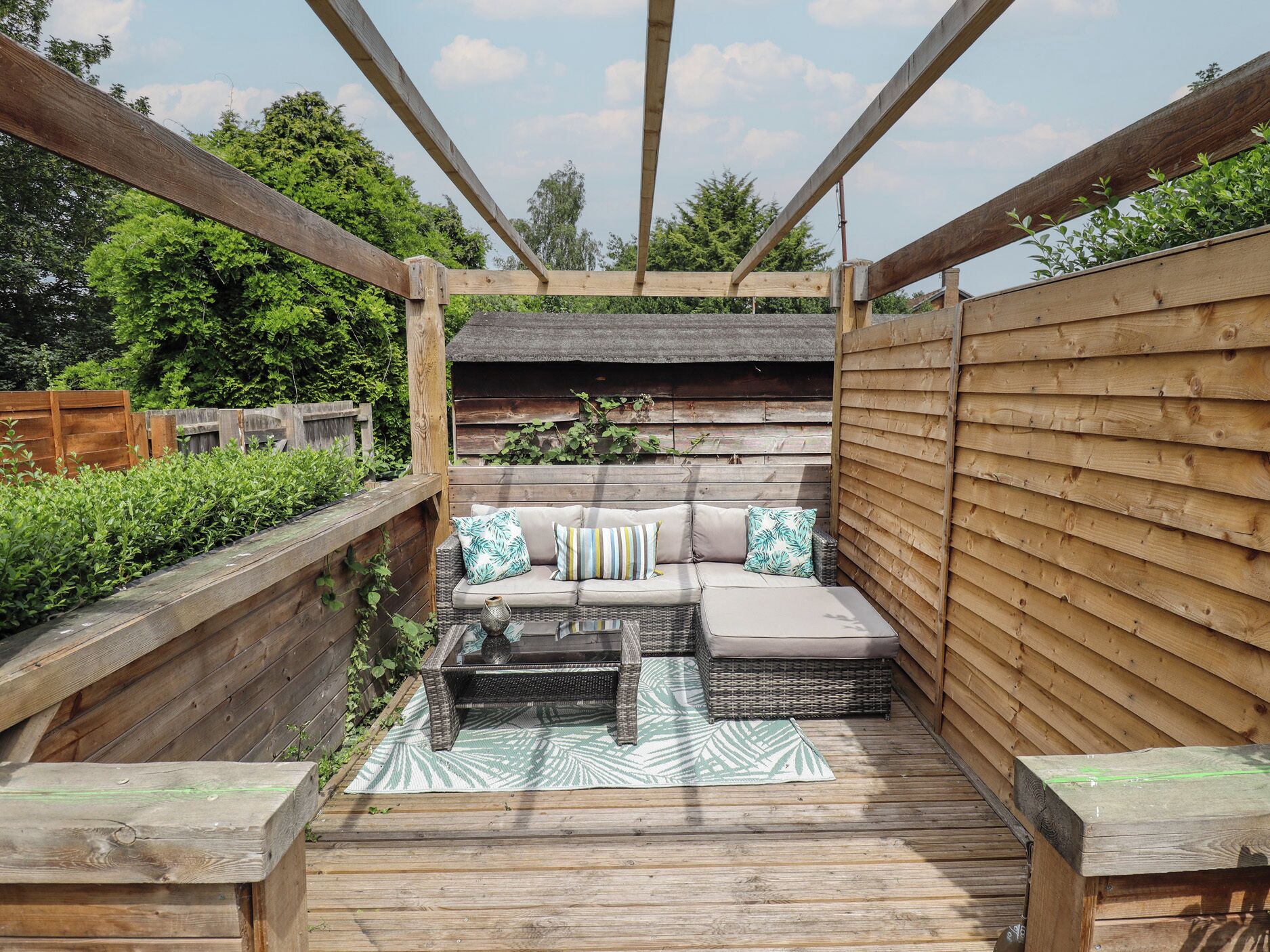 A wooden deck with a sofa and a table, surrounded by wooden railings and a wooden fence.