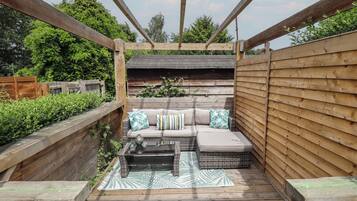 A wooden deck with a sofa and a table, surrounded by wooden railings and a wooden fence.