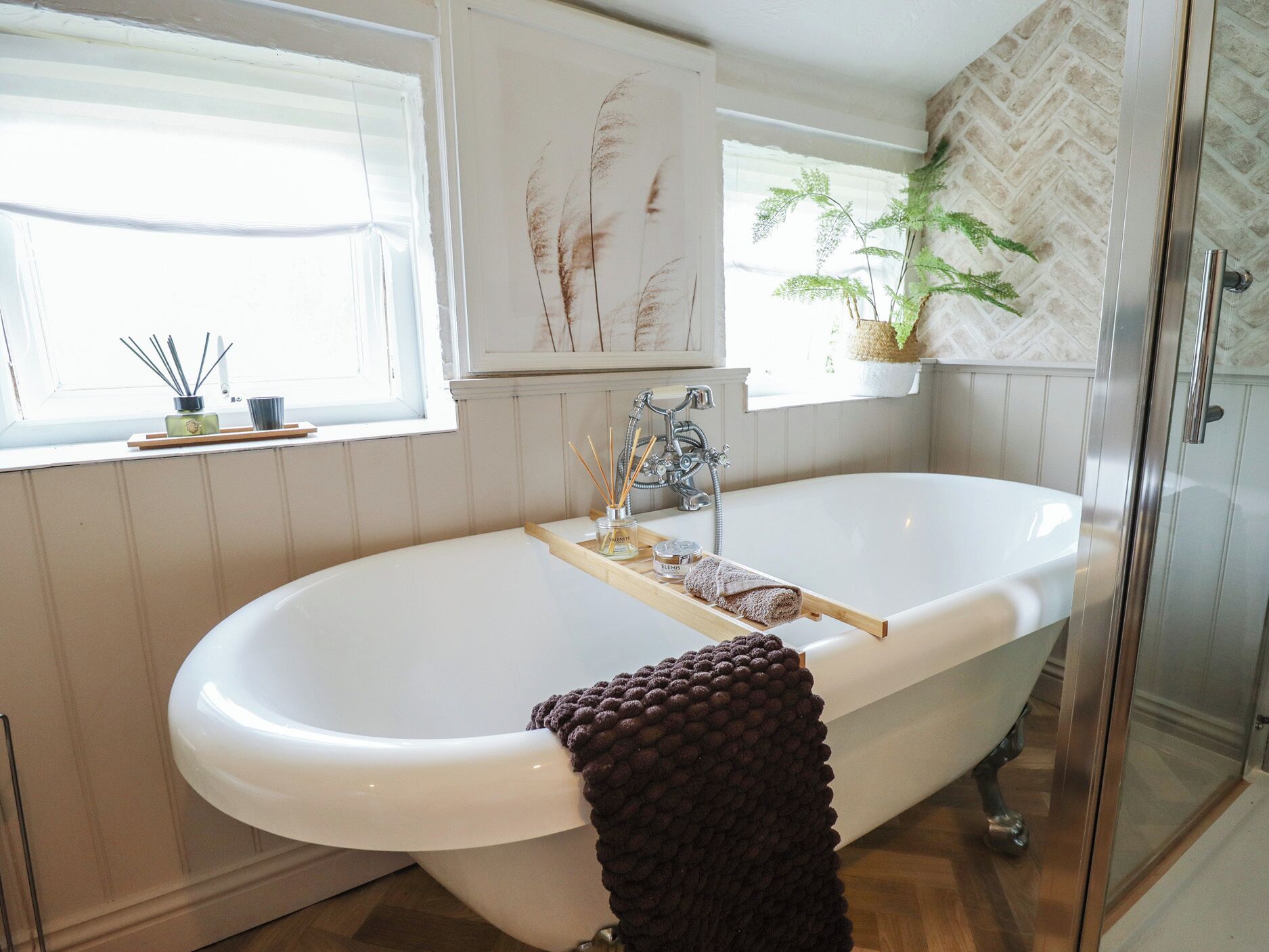 Une salle de bain avec une baignoire sur pieds, une douche à parois de verre et une fenêtre agrémentée d’une plante.