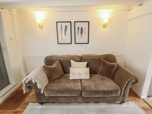 A brown sofa with a white throw blanket and pillows, two framed feather pictures on the wall, and a white radiator below. - Pax Cottage (Beccles)