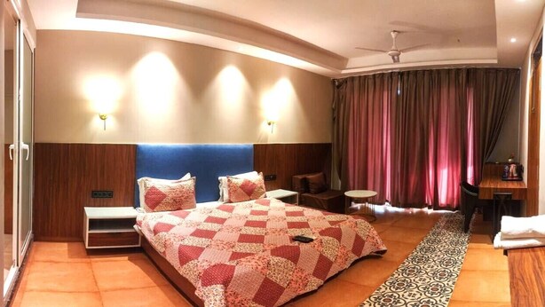 Ein Hotelzimmer mit einem großen Bett, zwei Nachttischen, einem Schreibtisch, einem Sessel und Blick ins Freie.