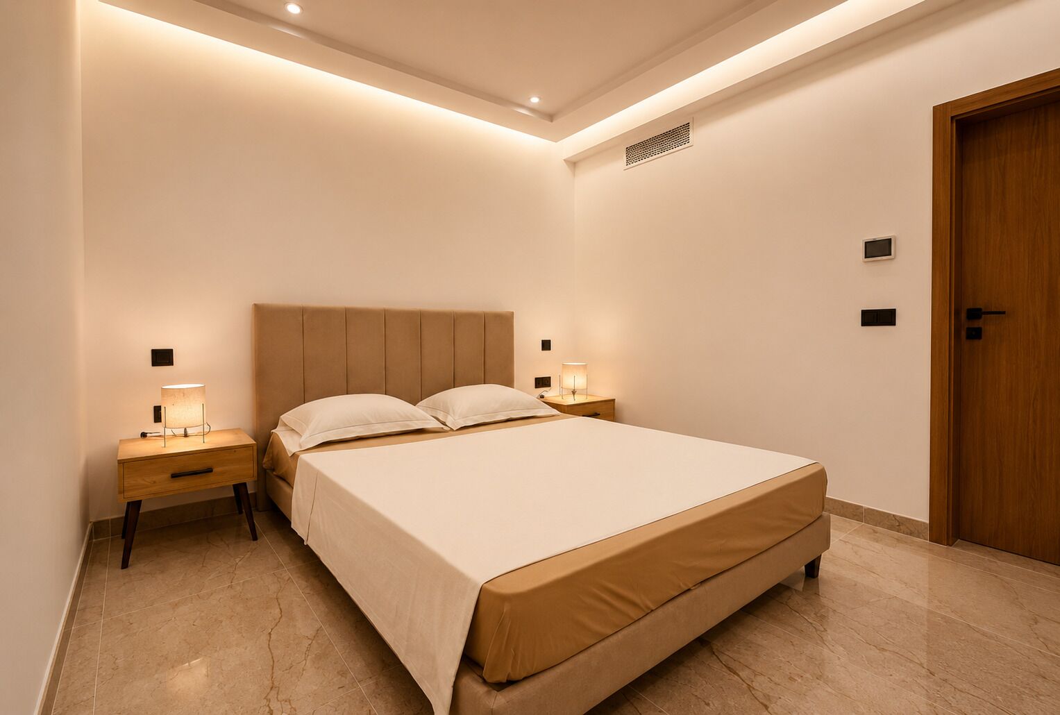 A bedroom with a bed, bedside lamps, a wooden nightstand, a wooden door, and a ceiling vent.