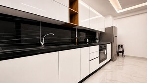 A modern kitchen with white cabinets, a black countertop, a built-in oven, and a wooden shelf. - Chic & Calme – Jardin de Carthage (Tunis)