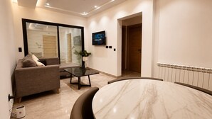 A modern living room with a sofa, a glass table, a marble coffee table, and a TV mounted on the wall. - Chic & Calme – Jardin de Carthage (Tunis)