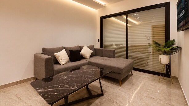 A modern living room with a sectional sofa, a marble coffee table, and a potted plant. - Chic & Calme – Jardin de Carthage (Tunis)