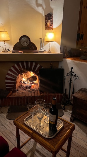 Ein gemütliches Zimmer mit Kamin aus Backsteinen, einer Uhr und einem Tisch mit Weingläsern und einer Weinflasche.
