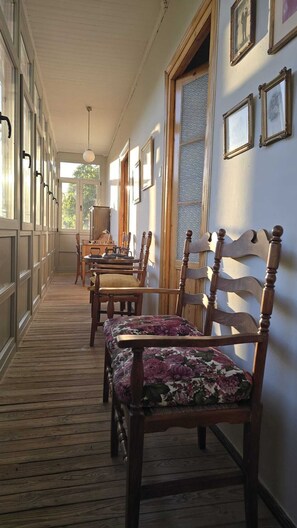 A corridor with wooden flooring, a wooden chair with a floral cushion, and a wooden table with a lamp.