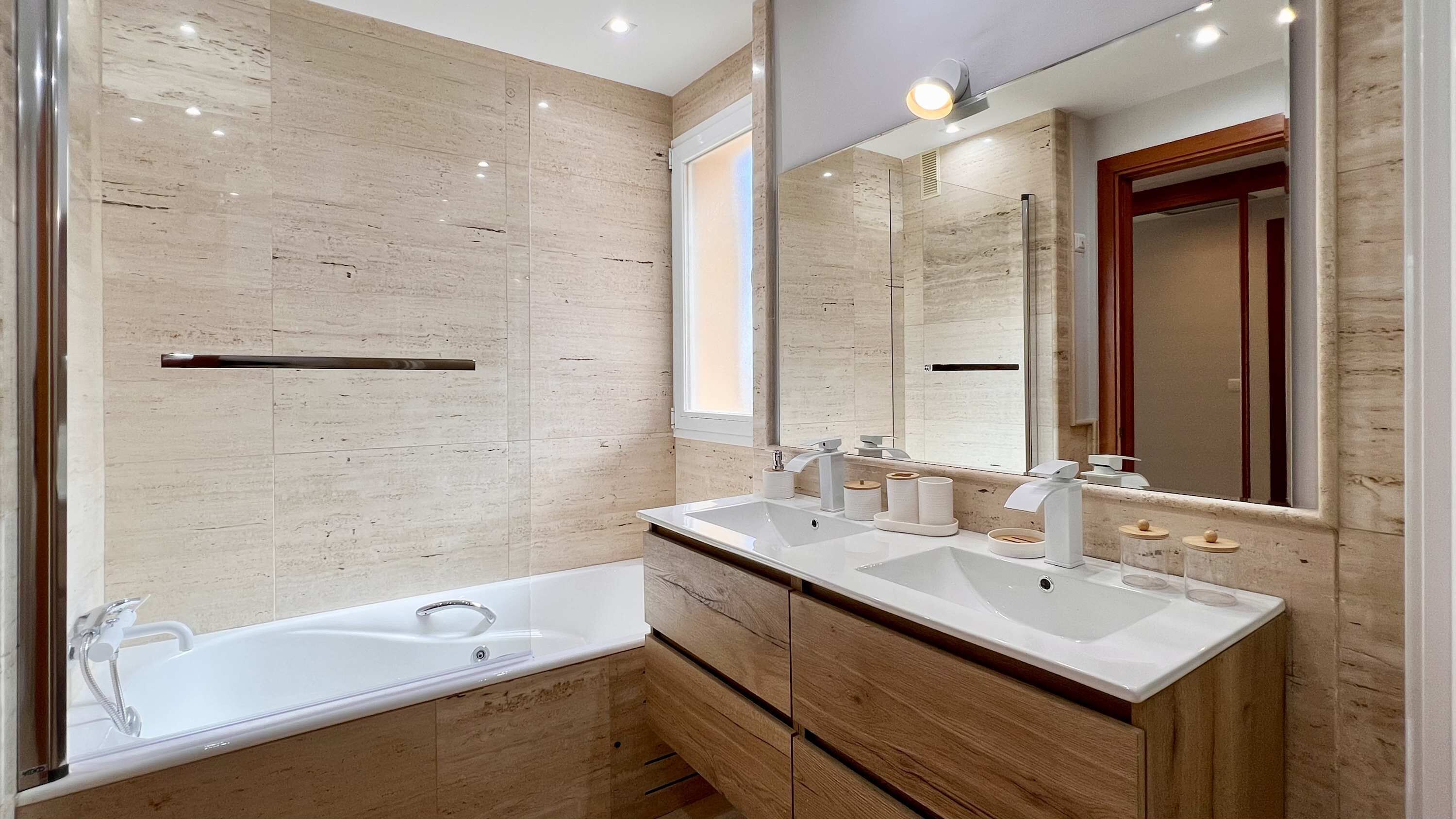 A modern bathroom with a double sink, a large mirror, and a bathtub.