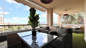 A balcony with wicker furniture, a glass table, and a large potted plant. - Relax Oasis and Terrace in Sol Andalusi (Alhaurín de la Torre)