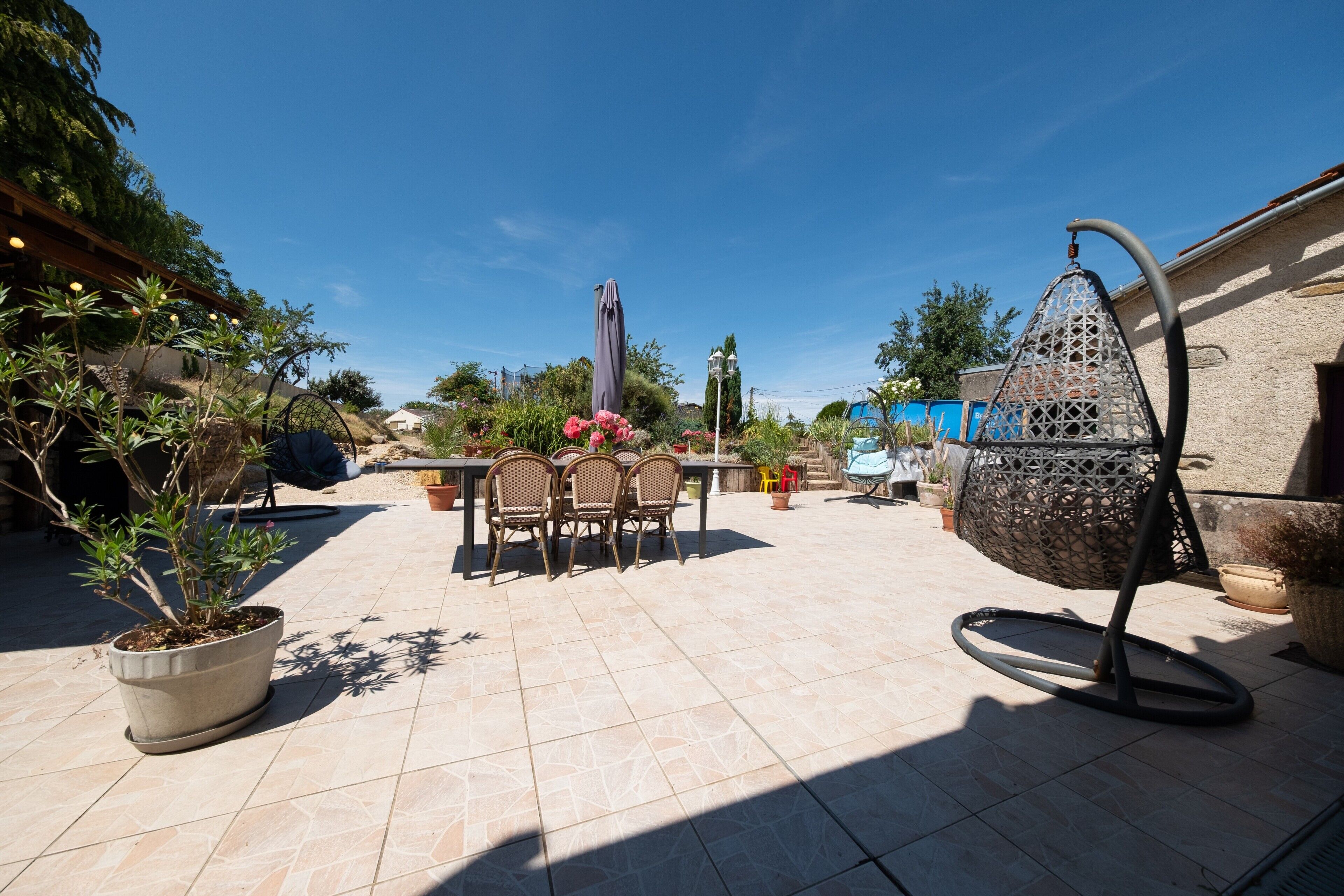 Un espace patio aménagé avec une table et des chaises, un fauteuil suspendu et des plantes en pot.