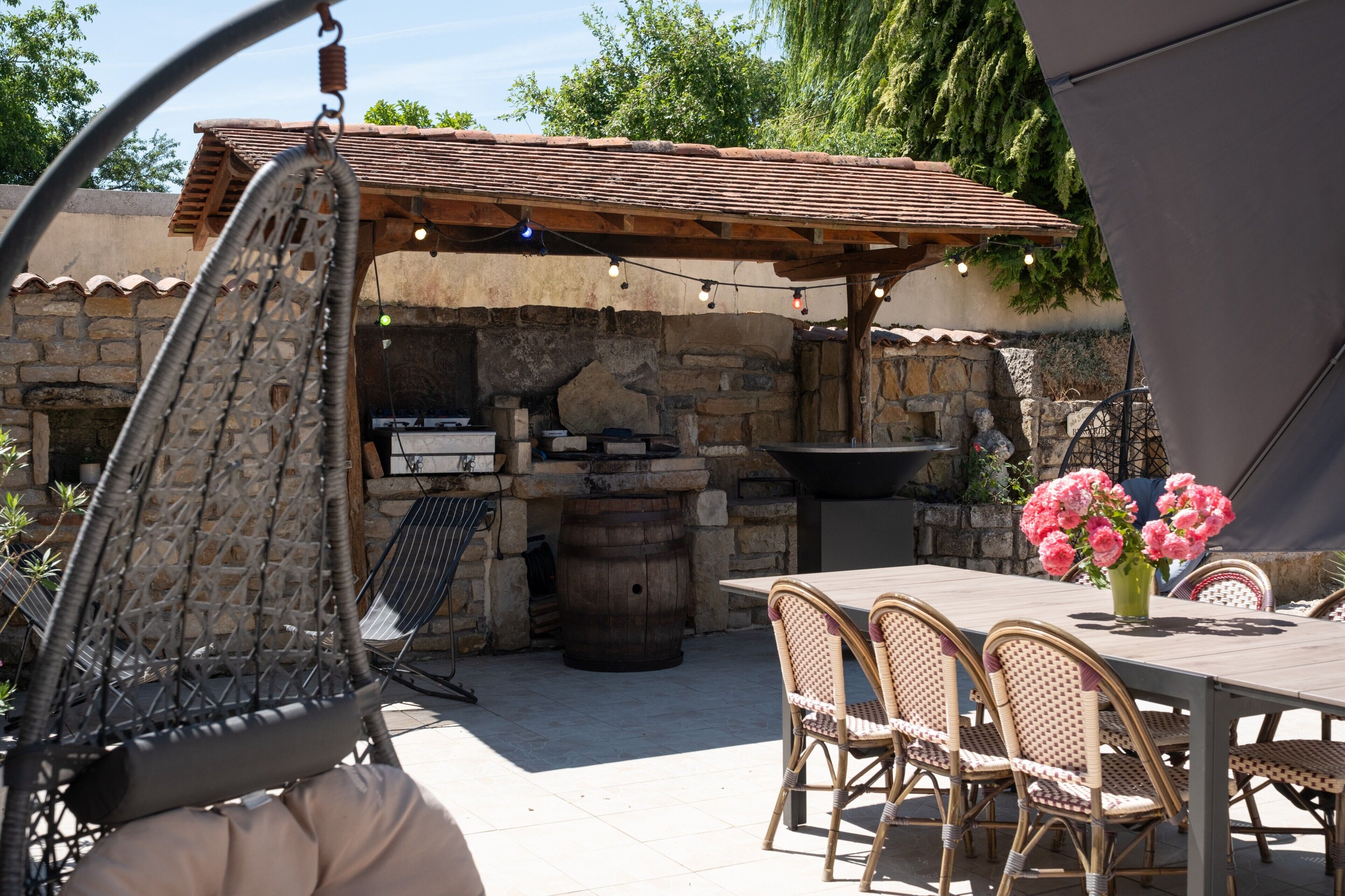 Un patio al aire libre con sillas de mimbre, una mesa con un florero y una pared de piedra con una parrilla.