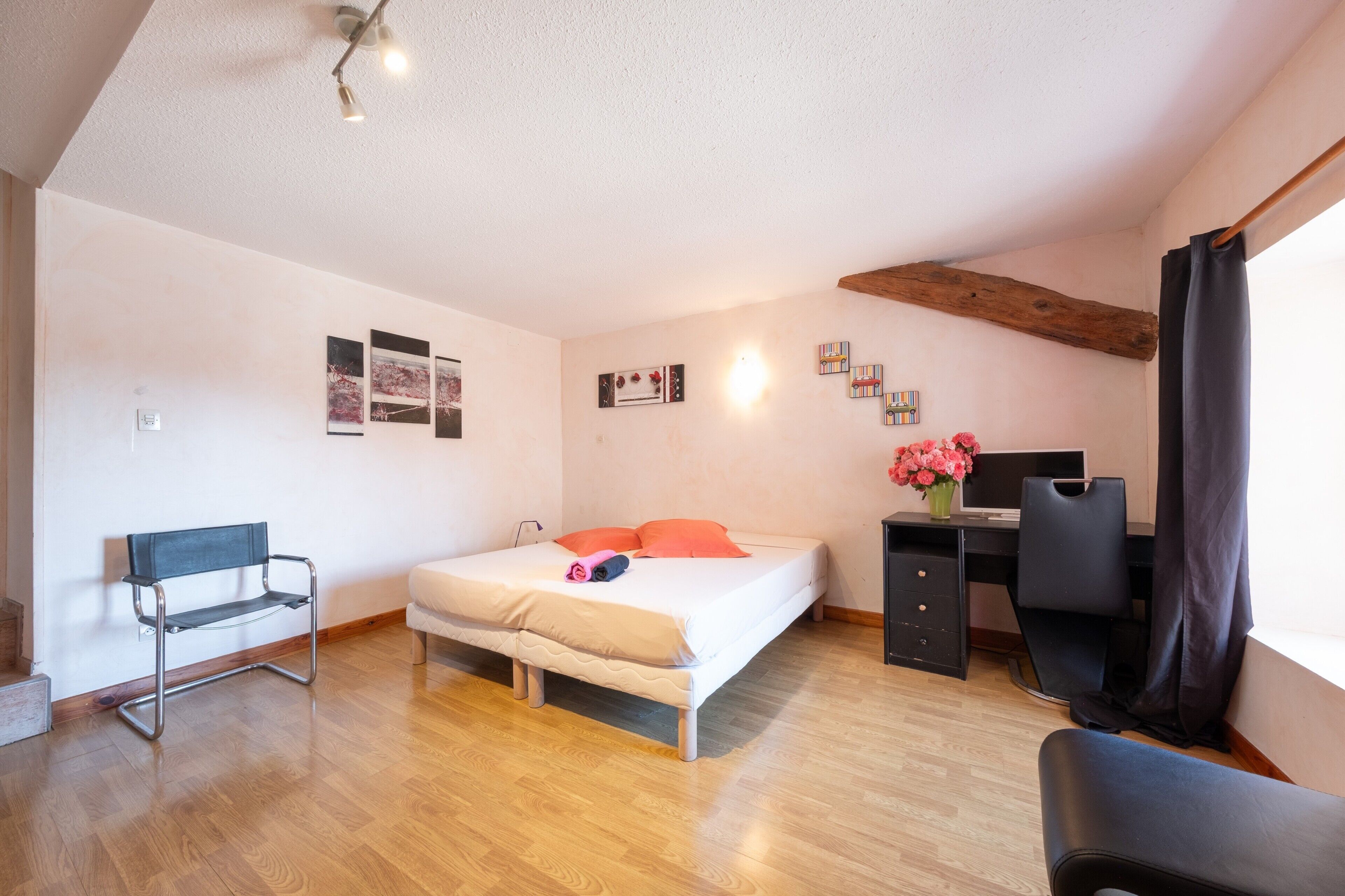 Une chambre à coucher avec un lit, un bureau, une chaise, un banc et une fenêtre avec des rideaux.