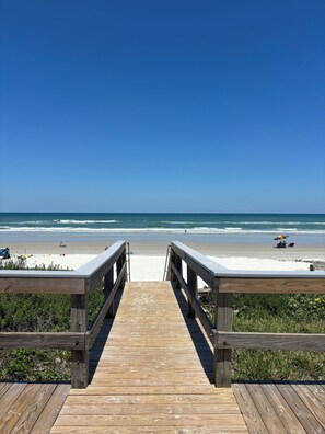 Une promenade en bois qui mène à une plage, avec un ciel bleu dégagé.