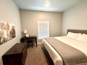 A bedroom with a bed, a desk, a chair, a lamp, and a window with blinds. - 106 Affordable College-Style Apartment, Grand National Parks (Rexburg)