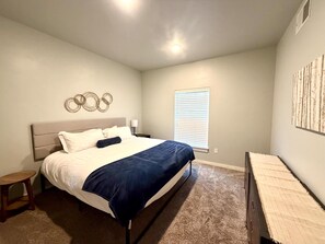Un dormitorio con cama, mesita de noche, ventana con persianas y decoración en la pared.