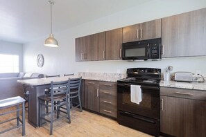 A modern kitchen with dark wood cabinets, a black stove, a microwave, and a dining area with chairs. - 204 Affordable College-Style Apartment, National Parks (Rexburg)