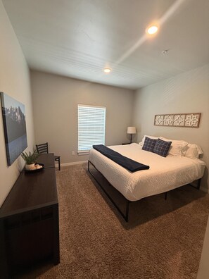 A bedroom with a bed, a desk, a chair, a window with blinds, and a ceiling light. - 206 Affordable College-Style Apartment, National Parks (Rexburg)