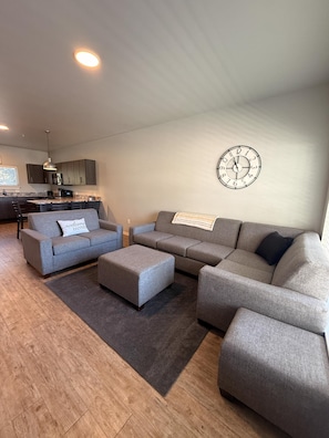 Ein modernes Wohnzimmer mit grauen Sofas, einem Couchtisch und einer Wanduhr.