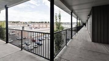A covered outdoor corridor with a concrete floor, metal railings, and a view of a parking lot and buildings in the distance.