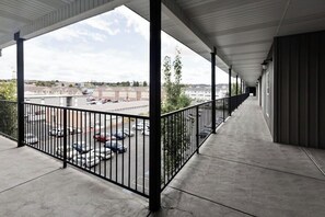 A covered outdoor corridor with a concrete floor, metal railings, and a view of a parking lot and buildings in the distance.