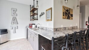 A modern kitchen with a marble island, bar stools, and a large 'EAT' sign on the wall.