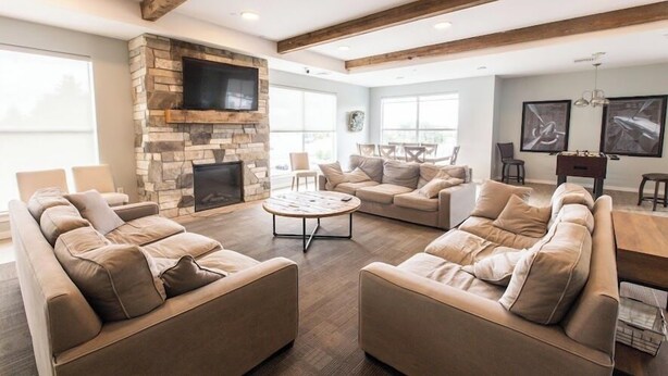 A spacious living room with a stone fireplace, multiple sofas, a coffee table, and a flat-screen TV mounted on the wall.