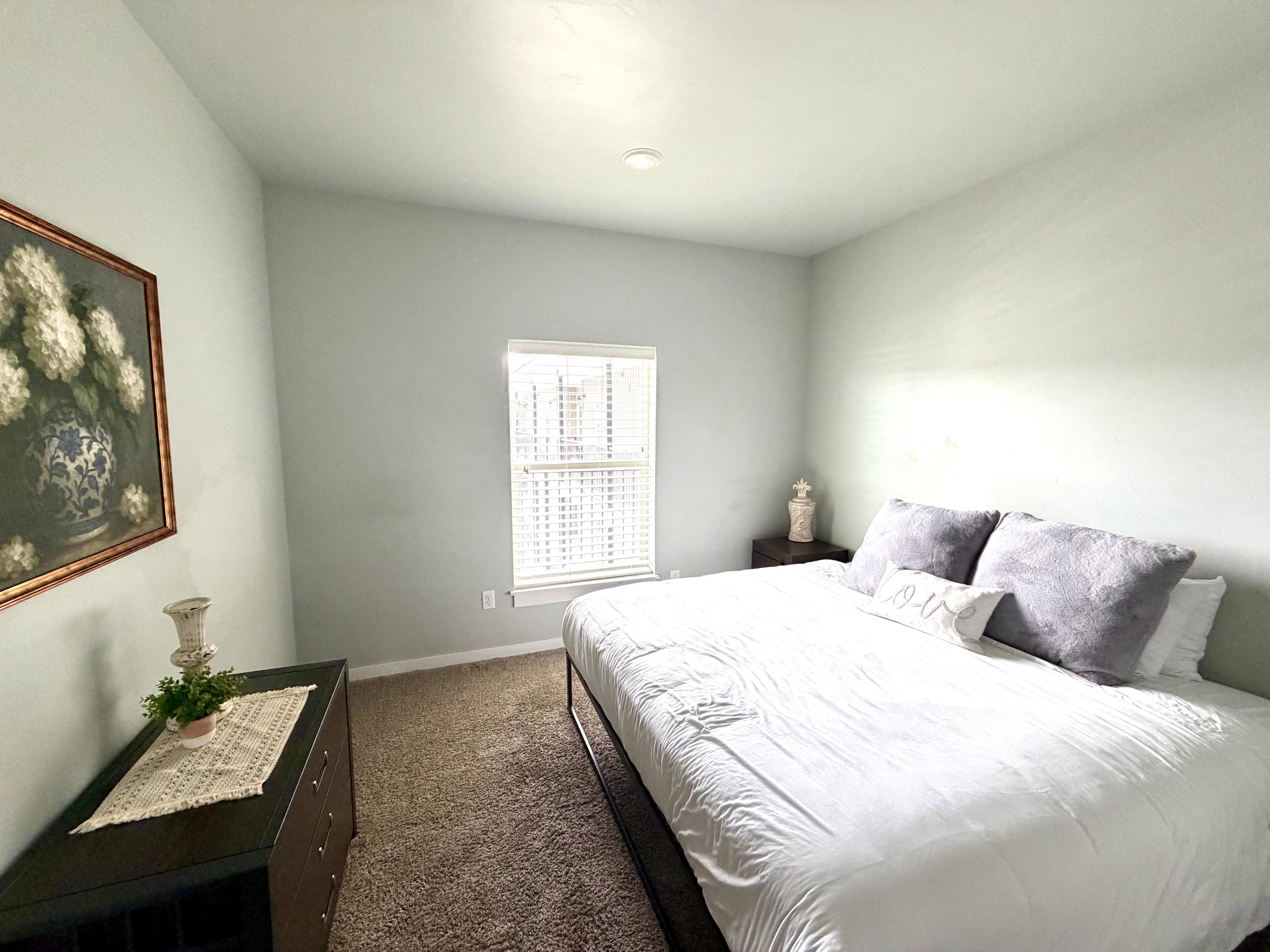 A bedroom with a bed, a nightstand, a window, and a painting on the wall.