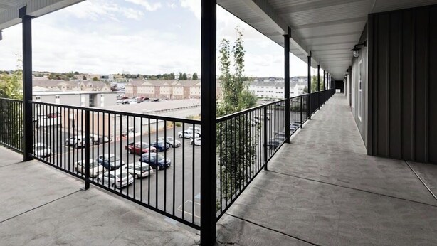 A covered outdoor corridor with a concrete floor, metal railings, and a view of a parking lot and buildings in the distance. - Brigham's Mill Retreat Between Grand Teton & Yellowstone National Parks (Rexburg)