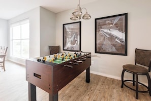 A room with a foosball table, two framed pictures on the wall, and a chair. - Brigham's Mill Retreat Between Grand Teton & Yellowstone National Parks (Rexburg)